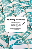 A close-up of many round pin-back buttons with a teal and white design reading 'Hello my name is'. A large white text box overlaid in the center says 'Quantity Discounts' with discount tiers and an arrow pointing to the buttons.